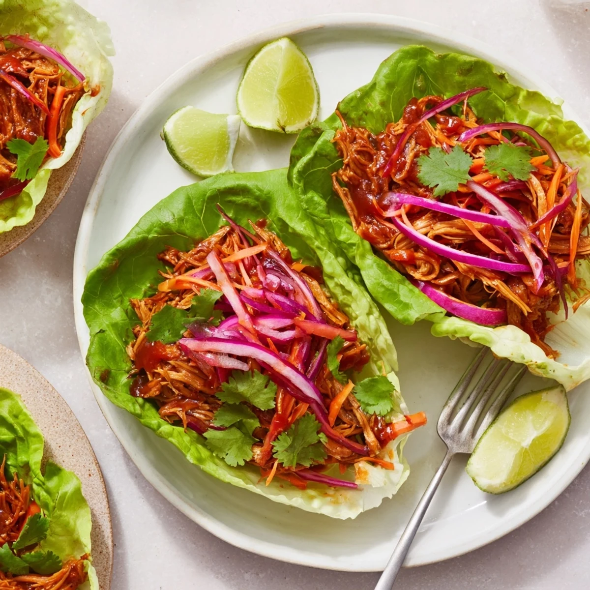 Tender BBQ jackfruit lettuce wraps garnished with fresh vegetables and lime wedges.  