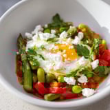 Serving suggestion for Pea and Broad Bean Shakshuka, featuring runny yolks, fresh mint, and feta, alongside crusty artisan bread for dipping.