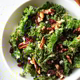 Warm maple mustard kale salad tossed with dried cranberries, crunchy toasted walnuts, and thin red onion slices ready to serve.