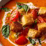 A bowl of soup with tomatoes and bread.