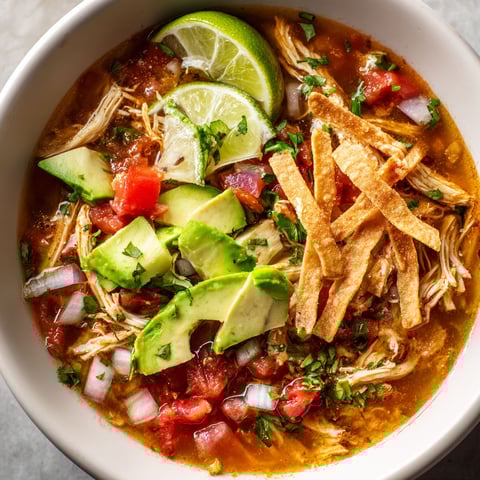 A bowl of chicken tortilla soup with chips on top.