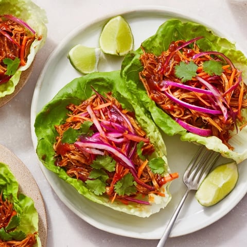 Tender BBQ jackfruit lettuce wraps garnished with fresh vegetables and lime wedges.  