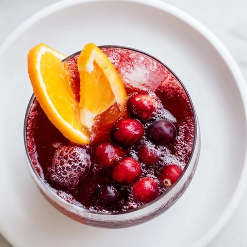 Refreshing 3-Ingredient Holiday Punch in a glass, garnished with bright orange slices and cranberries.