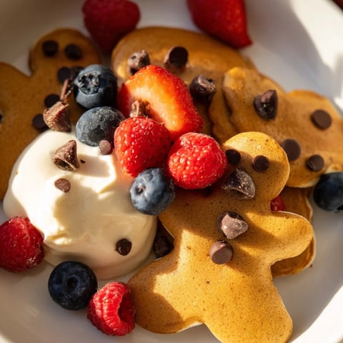 Gingerbread Boy Berry Board with warm gingerbread pancakes, fresh berries, and creamy yogurt, perfect for breakfast.