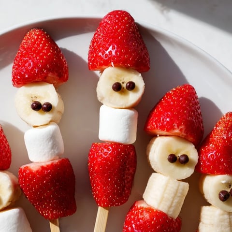 Vibrant Strawberry Banana Santa Sticks, a festive snack with fresh fruit and fluffy marshmallows arranged on skewers.