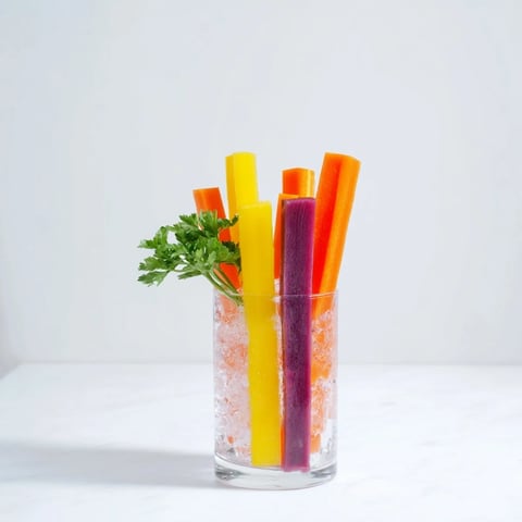Rainbow carrot sticks, a colorful and healthy crudités appetizer, served chilled in tall glasses.