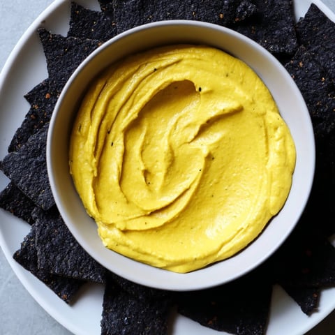 Vibrant Midnight Sun appetizer: Creamy carrot dip encircled by crispy black charcoal crackers for snacking.