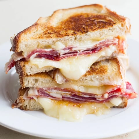 Golden, gooey Charcuterie Grilled Cheese sandwich with melted cheese and savory meats on display.