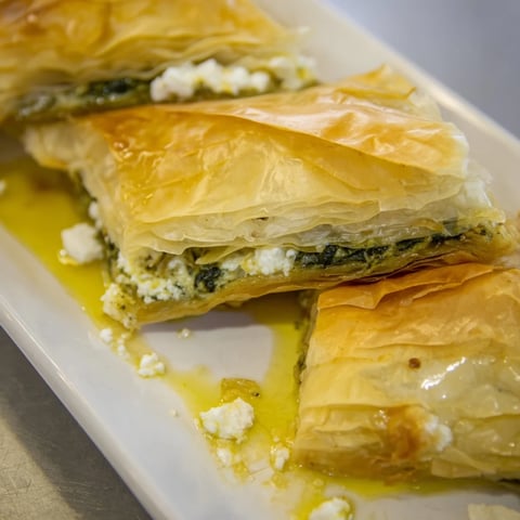 Golden, flaky Greek spanakopita, revealing a savory spinach and feta filling, ready to serve.