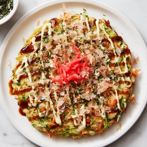 Golden-brown Japanese Okonomiyaki pancake topped with sauce, mayo, dancing bonito flakes, ready to enjoy.
