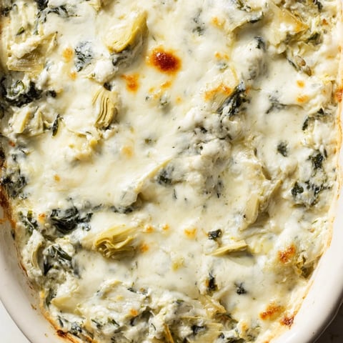 Creamy spinach artichoke dip in a golden baking dish, paired with crispy tortilla chips for dipping.  