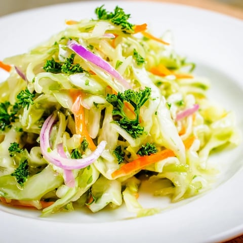 A vibrant plate of Cooked and Loved Cabbage Salad features sautéed cabbage tossed with crisp carrots and red onions, dressed in a tangy apple cider vinaigrette.  