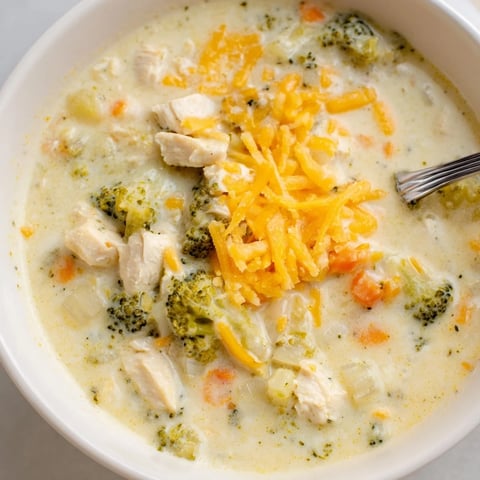Creamy Best Chicken Broccoli Cheddar Soup steaming in a rustic bowl, with tender chicken, green broccoli florets, and melted cheddar visible.  