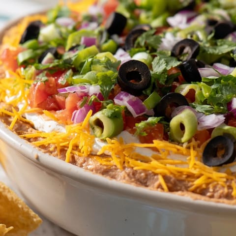 A close-up of the 4-Way Layered Dip, topped with shredded cheddar, olives, and fresh green onions.  