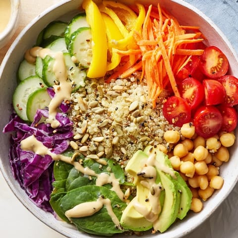 Vibrant Rainbow Buddha Bowl With Quinoa features quinoa, chickpeas, and fresh veggies drizzled with tahini dressing.