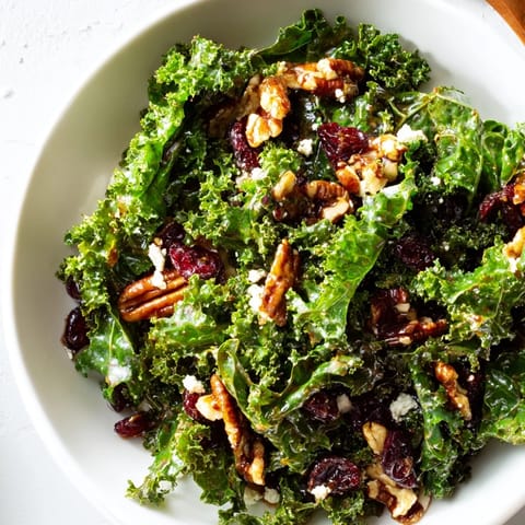 Warm maple mustard kale salad tossed with dried cranberries, crunchy toasted walnuts, and thin red onion slices ready to serve.