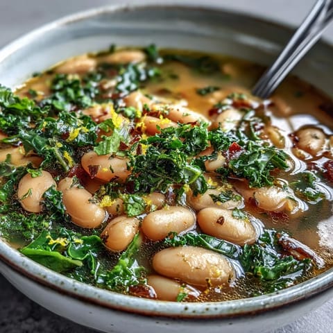A steaming bowl of Tuscan white bean soup with tender kale and fresh lemon zest, garnished with Parmesan and olive oil.  