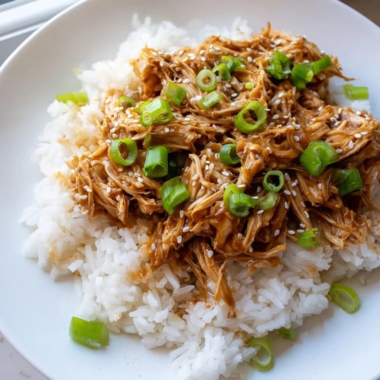 Steaming white rice topped with saucy Easy Slow Cooker Teriyaki Chicken, garnished with fresh green onions.
