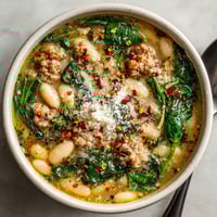 A bowl of soup with beans, spinach, and meat.